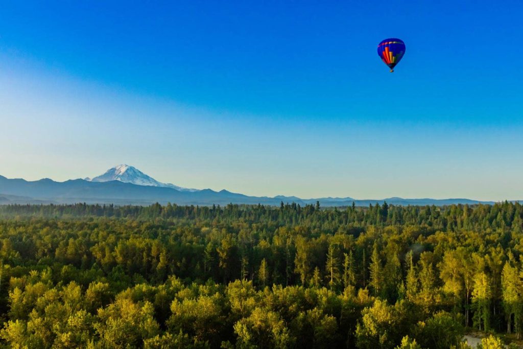 Hot air balloon rising over the trees to show the view of Mt. Rainier.