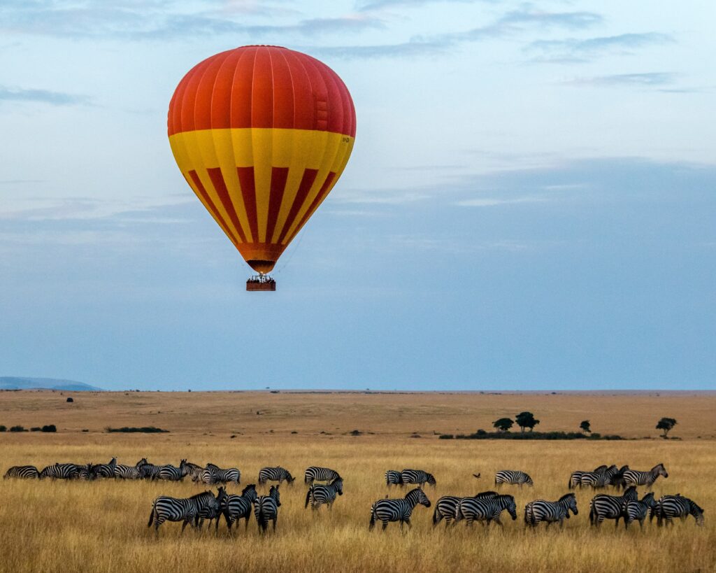 Red hot air balloon drifting over the Serengeti over a field of zebras.