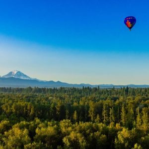 Hot air balloon rising over the trees to show the view of Mt. Rainier