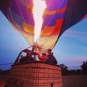 Looking up at a hot air balloon envelope with the burner firing. Fabric is blue, pink, yellow, purple