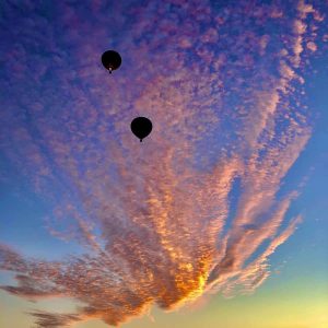 Pink, purple, and blue sunrise with scattered clouds and two hot air balloons