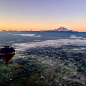 View from a hot air balloon at sunrise as the sun is peeking over the Cascade mountains. A few stratus clouds and yellow light