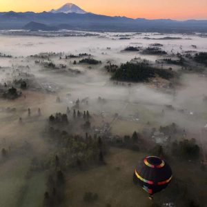 Pre-dawn view of Mt. Rainier from a hot air balloon. A thin layer of fog on the ground with an orange and pink glowing sky